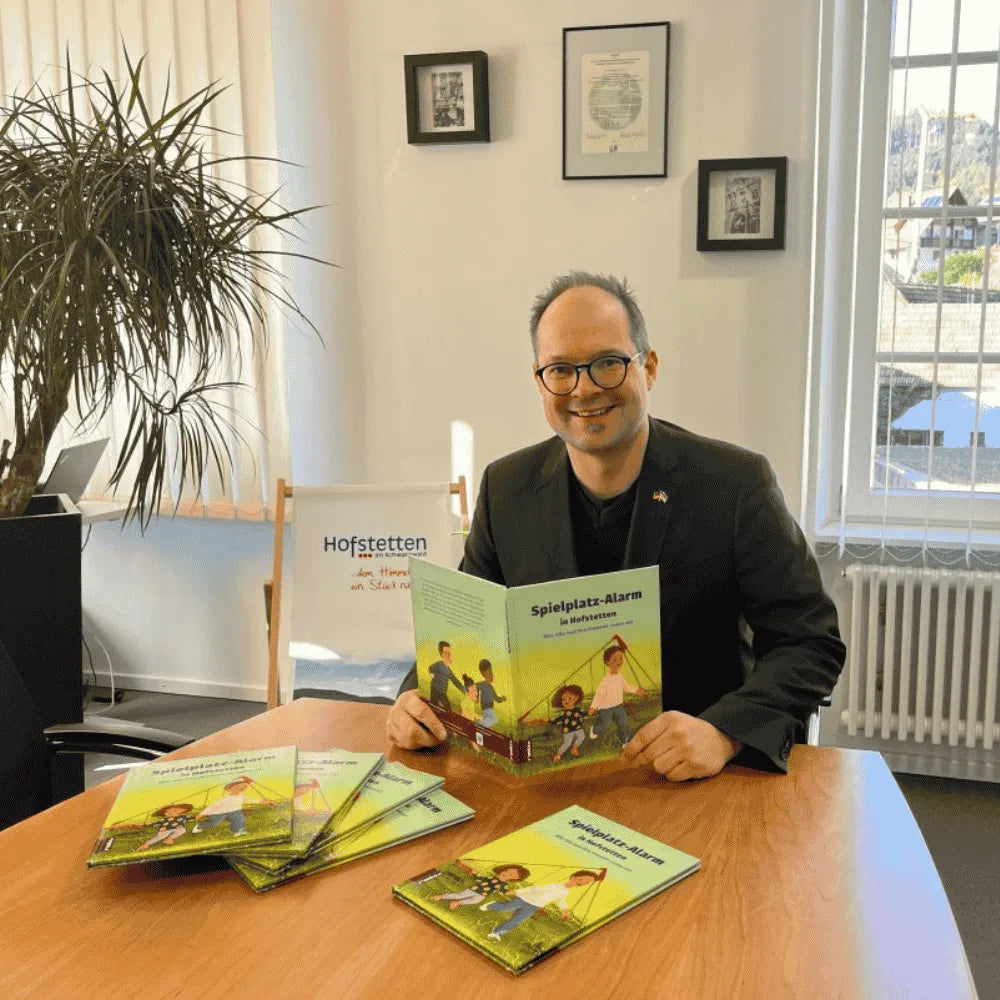 Bürgermeister hält lächelnd das Buch Spielplatz-Alarm in Hofstetten in der Hand