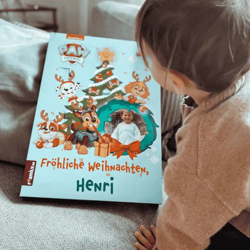 Ein Kind bewundert den Framily PAW Patrol Adventskalender, mit der Paw Patrol, einem Weihnachtsbaum und dem Gruß "Fröhliche Weihnachten, Henri".