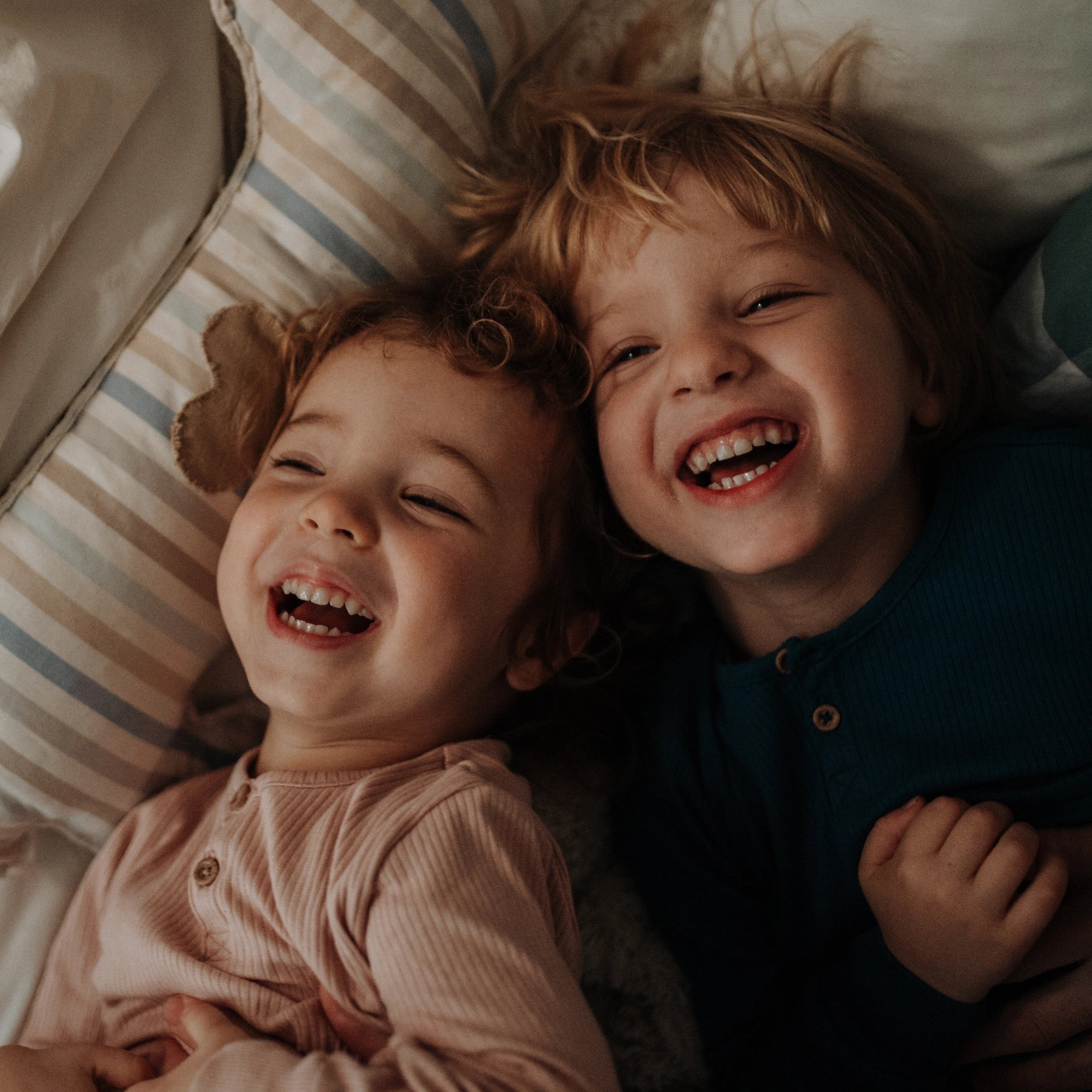 Zwei Geschwisterkinder kuscheln und lachen im Bett liegend